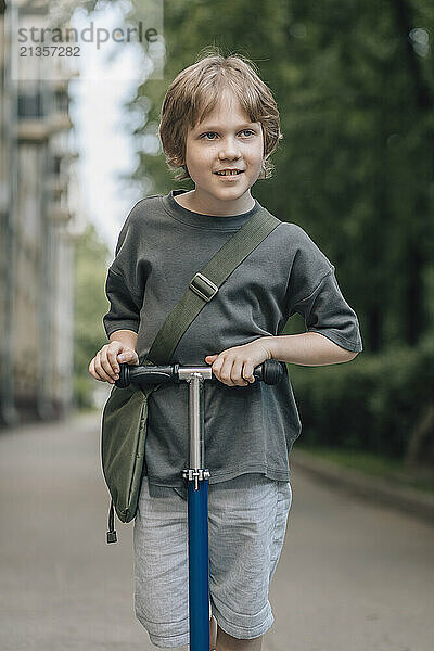 Smiling boy standing with push scooter on street