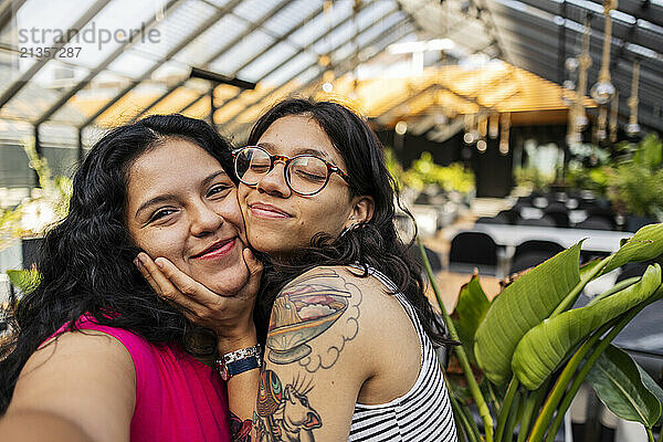 Smiling woman taking selfie with girlfriend wearing eyeglasses at cafe