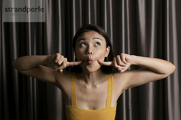 Playful woman in sleeveless yellow top puckering in front of curtain at photo booth