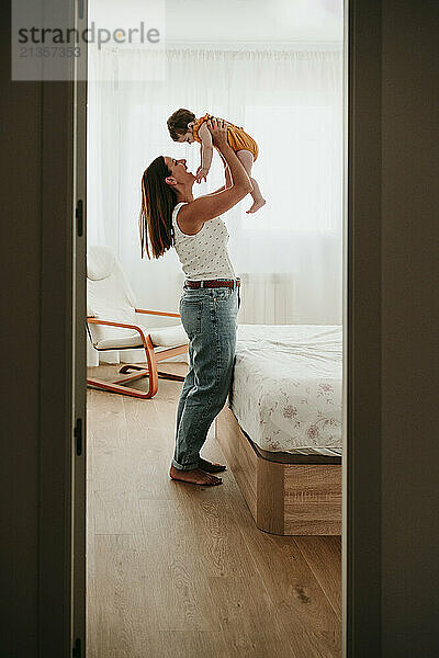 Carefree mother playing and picking up daughter in bedroom at home