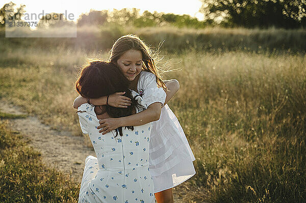 Happy girl hugging mother on field at sunset