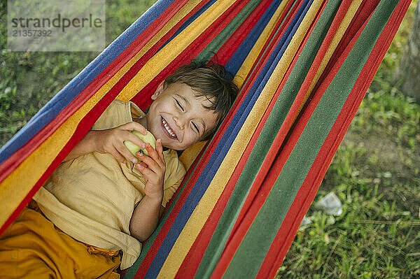 Smiling boy with eyes closed lying in colorful hammock