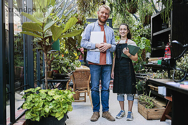 Smiling couple standing with wireless technologies at greenhouse