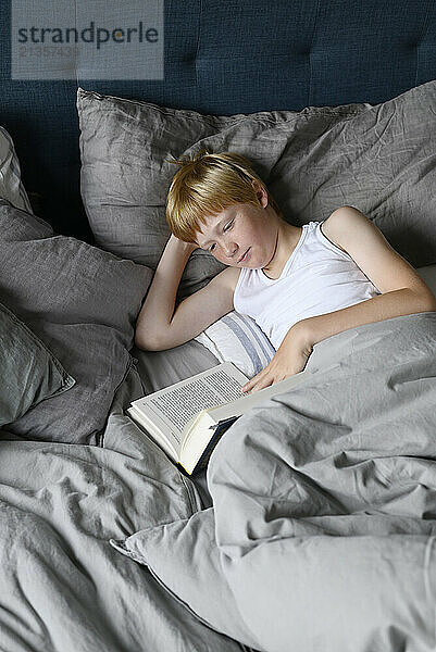 Boy lying on bed and reading book at home