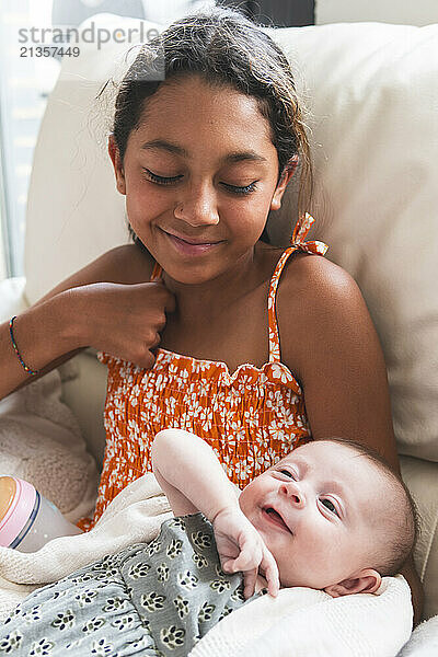 Smiling girl looking at baby and sitting on sofa