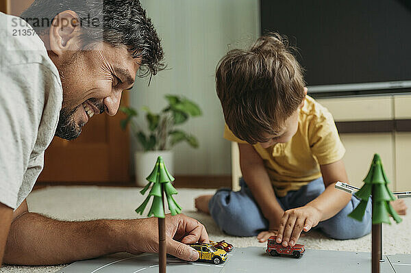 Smiling father and son spending leisure time playing with toy cars at home