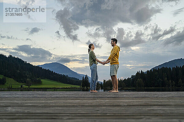 Smiling man and woman looking at each other and holding hands on jetty