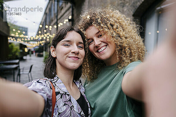 Smiling lesbian couple taking selfie in front of building