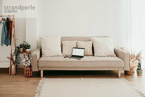 Home interior of laptop on sofa near plants with carpet