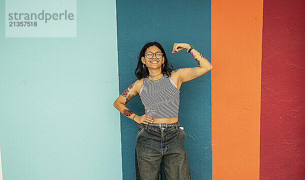 Happy woman flexing muscles near striped wall