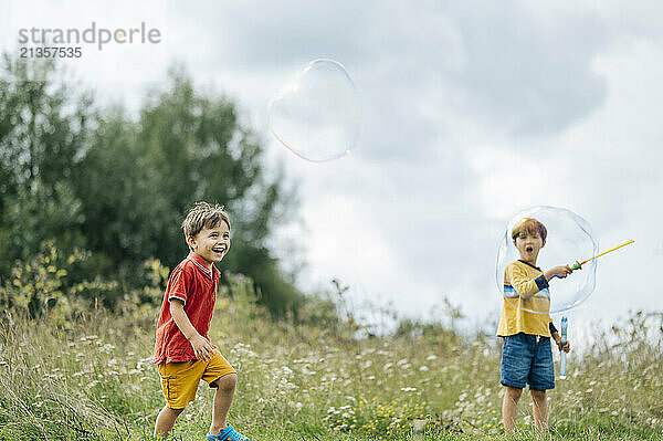 Happy boys playing with bubbles together in field