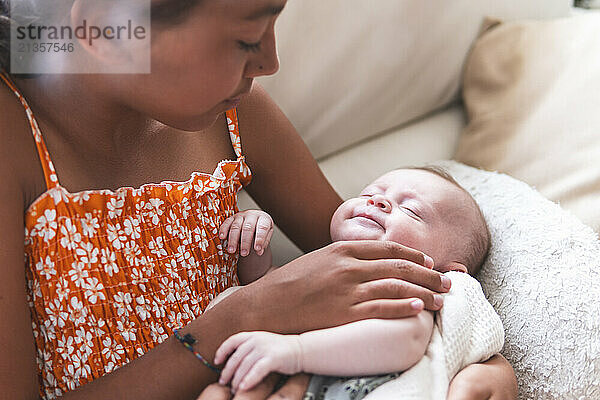 Sister looking at baby girl and resting on sofa