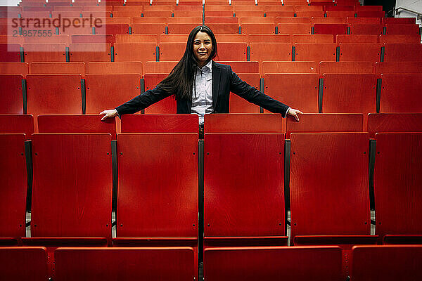 Smiling businesswoman amidst red seats in auditorium