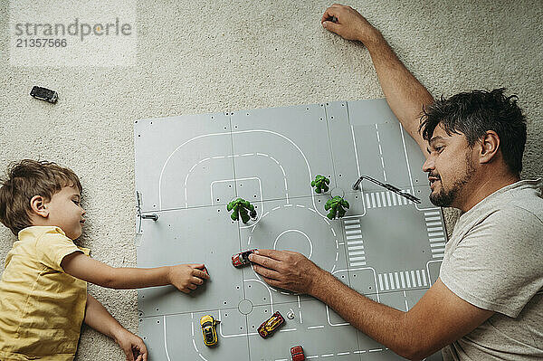 Father and son lying down and playing with toy cars at home