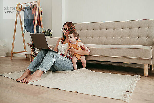 Businesswoman working on laptop and sitting with daughter at home