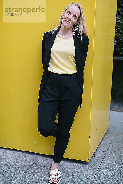 Smiling businesswoman leaning on yellow wall