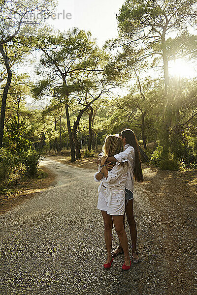 Teenage girl embracing mother from behind standing on road in forest