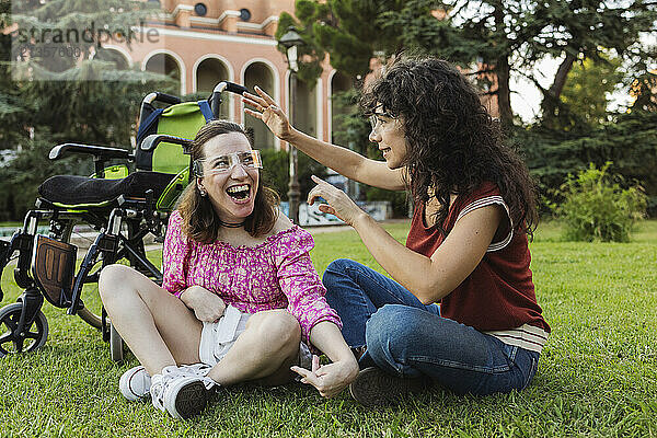 Assistant nurse and woman with physical disability wearing smart glasses and sitting on grass