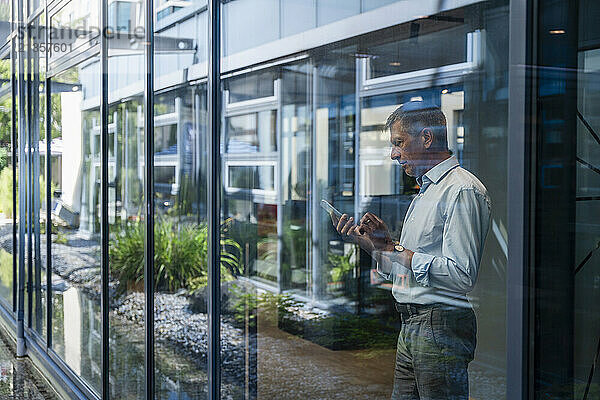 Businessman using smart phone seen through glass