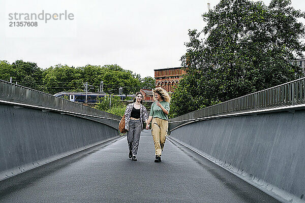 Lesbian couple holding hands and walking on bridge