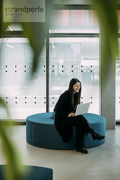 Happy businesswoman sitting on seat with laptop in office