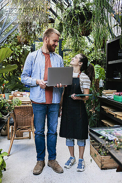 Happy couple standing with wireless technologies at greenhouse