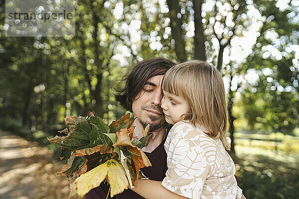 Father and daughter with autumn leaves hugging each other in park