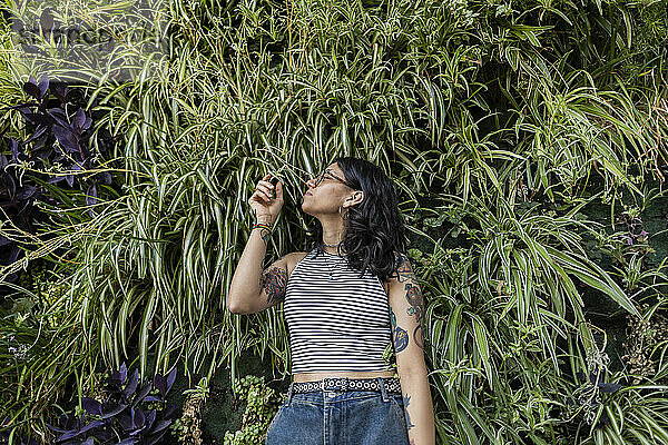 Young woman with tattooed arm standing in front of grass wall