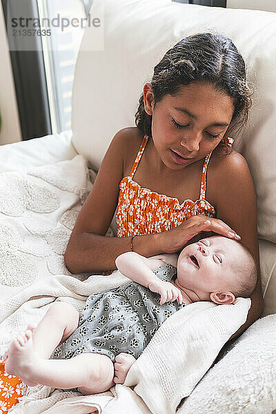 Innocent girl napping with baby on sofa at home