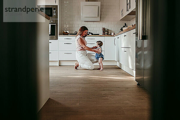 Mother playing with baby girl in kitchen at home