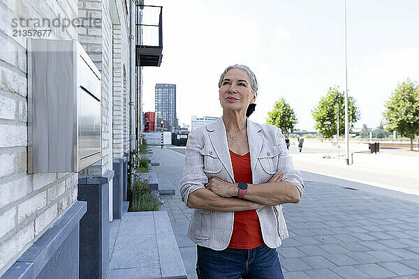 Confident senior woman with arms crossed standing near building