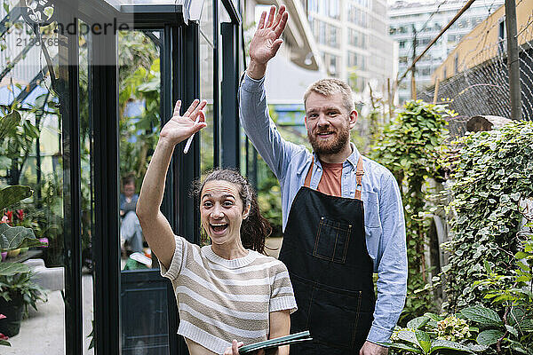 Couple with hand raised waving and standing in greenhouse