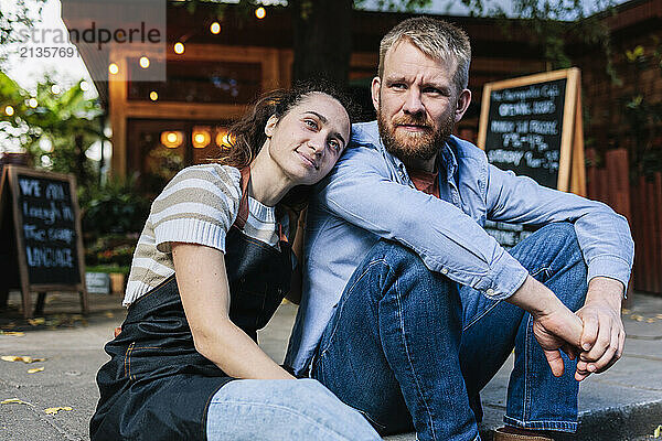 Young cafe owner leaning on boyfriend sitting outside cafe