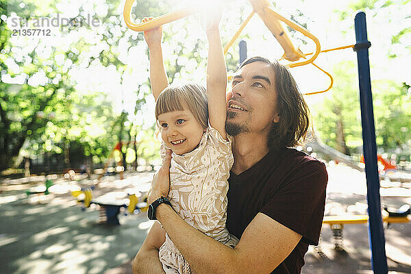 Father helping daughter holding monkey bars at playground