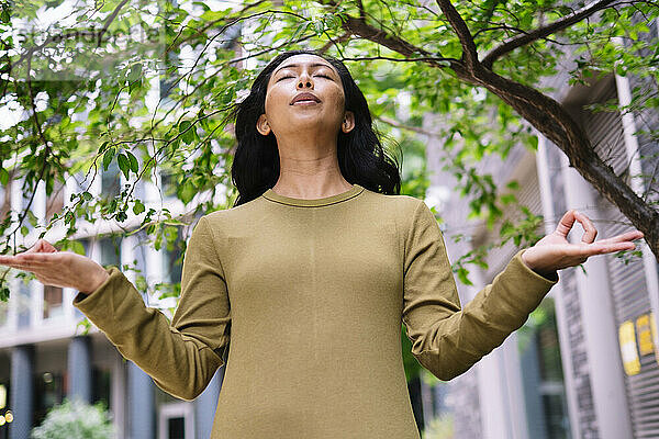 Woman meditating near tree in front of building