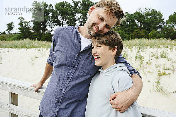 Affectionate father with son standing near railing at beach