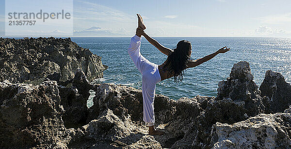 Yoga instructor doing bow pose at cliff of Mt Agung near ocean