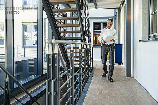 Businessman using tablet PC and walking near corridor in office