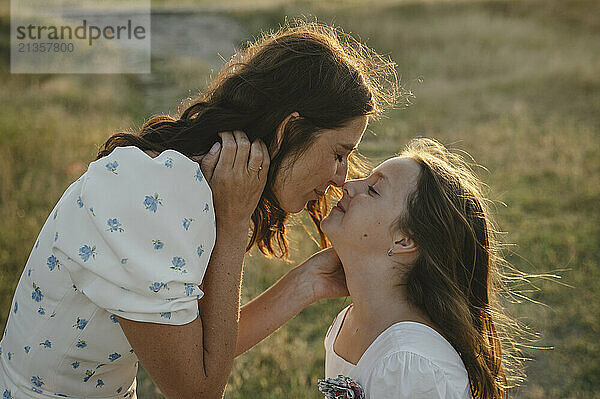 Smiling mother and daughter rubbing noses at field