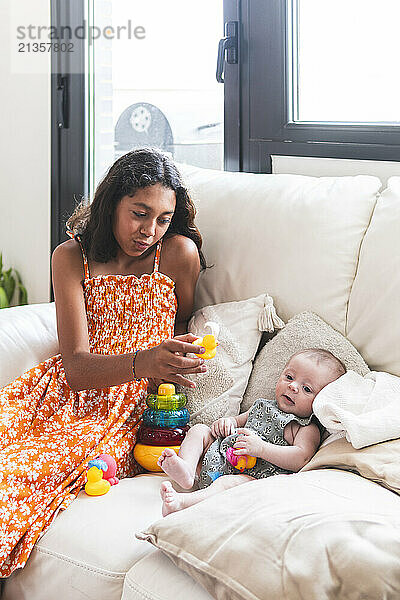 Sister showing toys to baby girl on sofa at home