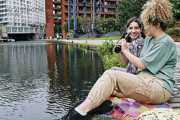 Happy lesbian couple having beer near river in city