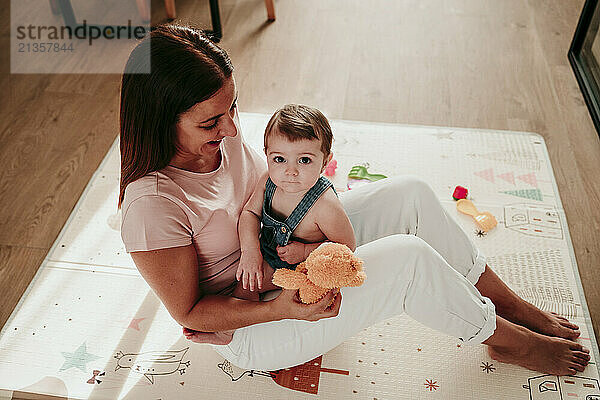 Happy woman sitting with baby daughter on rug at home