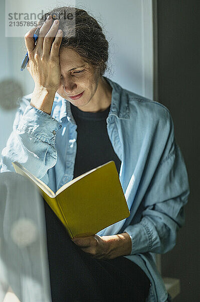 Worried woman reading diary at window in home