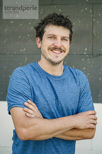 Happy worker standing with arms crossed in front of wall