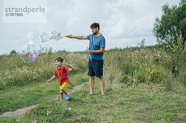 Father playing with soap bubbles and son running in field