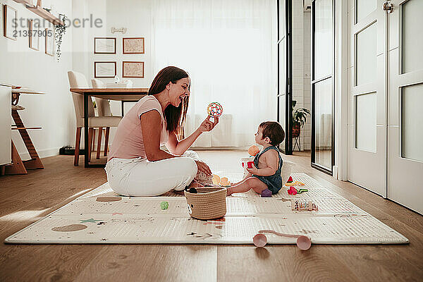 Mother and daughter playing with toys sitting on rug at home