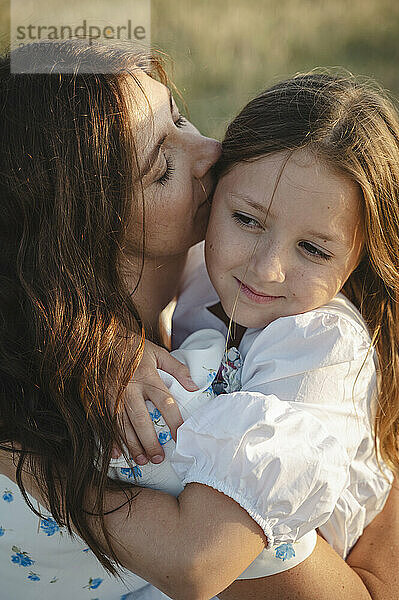 Mother kissing happy daughter on field