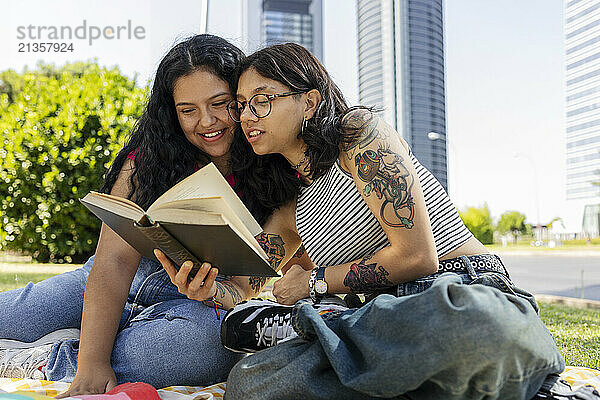 Young gay couple spending leisure time reading book sitting at park