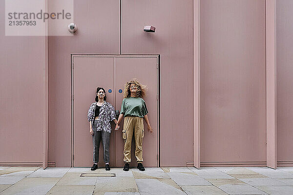 Happy lesbian couple standing in front of pink colored building door