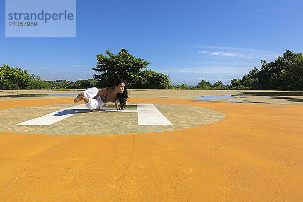 Yoga teacher doing grasshopper pose at public park under blue sky